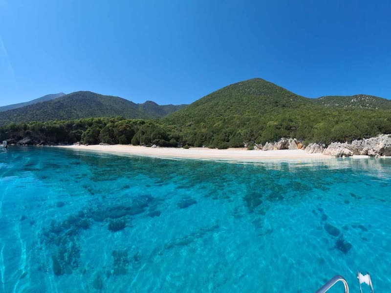 Shallow turquoise water and a white beach below green hills at Koutsoupia